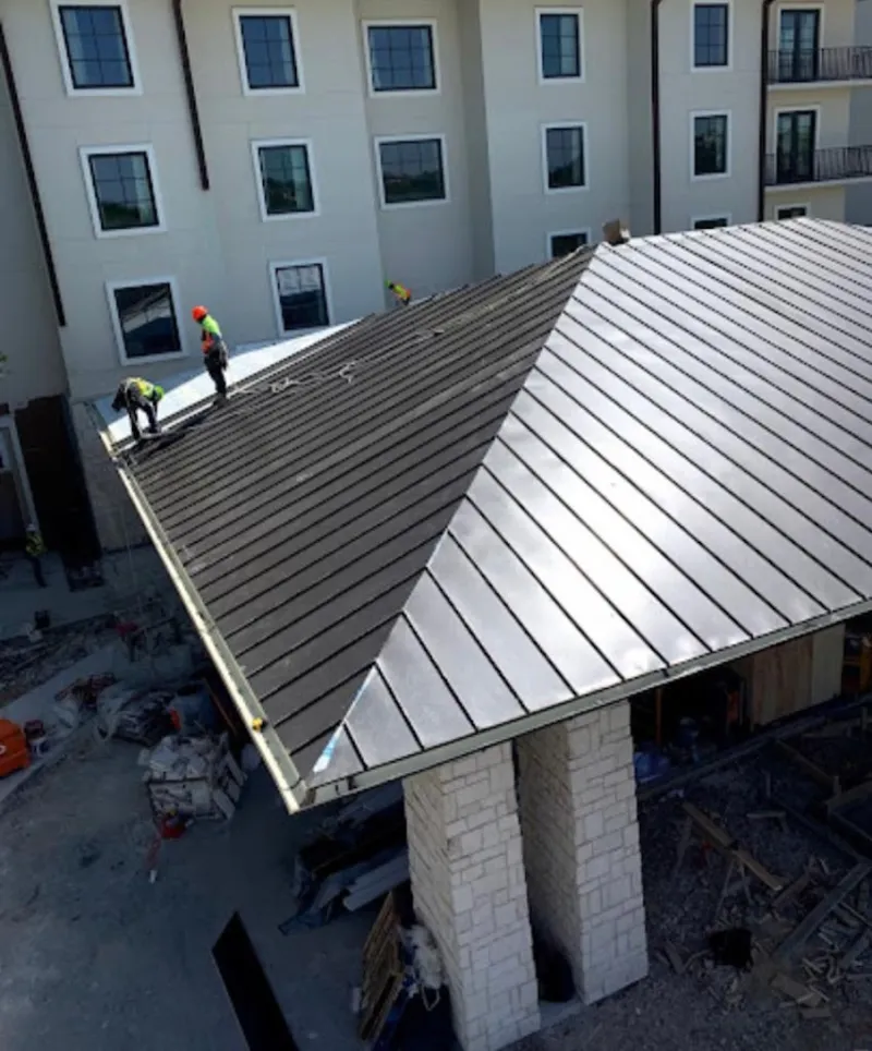 Crew installing standing seam metal roof panels on a commercial project in Novi
